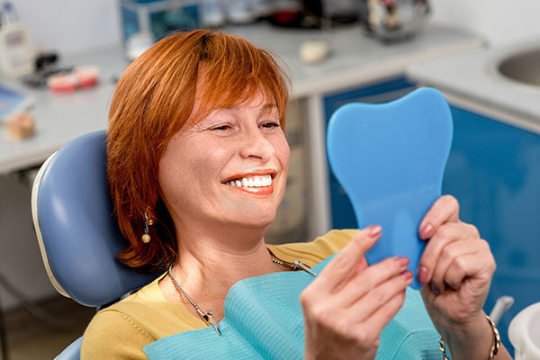 woman looking at dentures in mirror and smiling