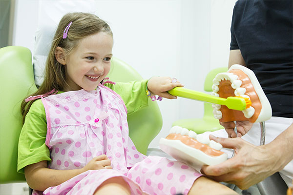 little girl playing with oversized toothbrush and model of teeth before pediatric dentistry