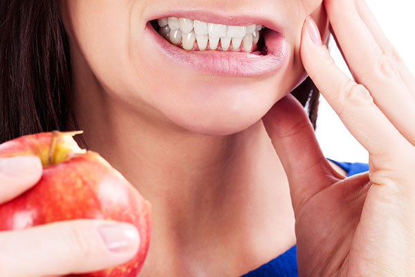 woman wincing eating an apple needs root canals